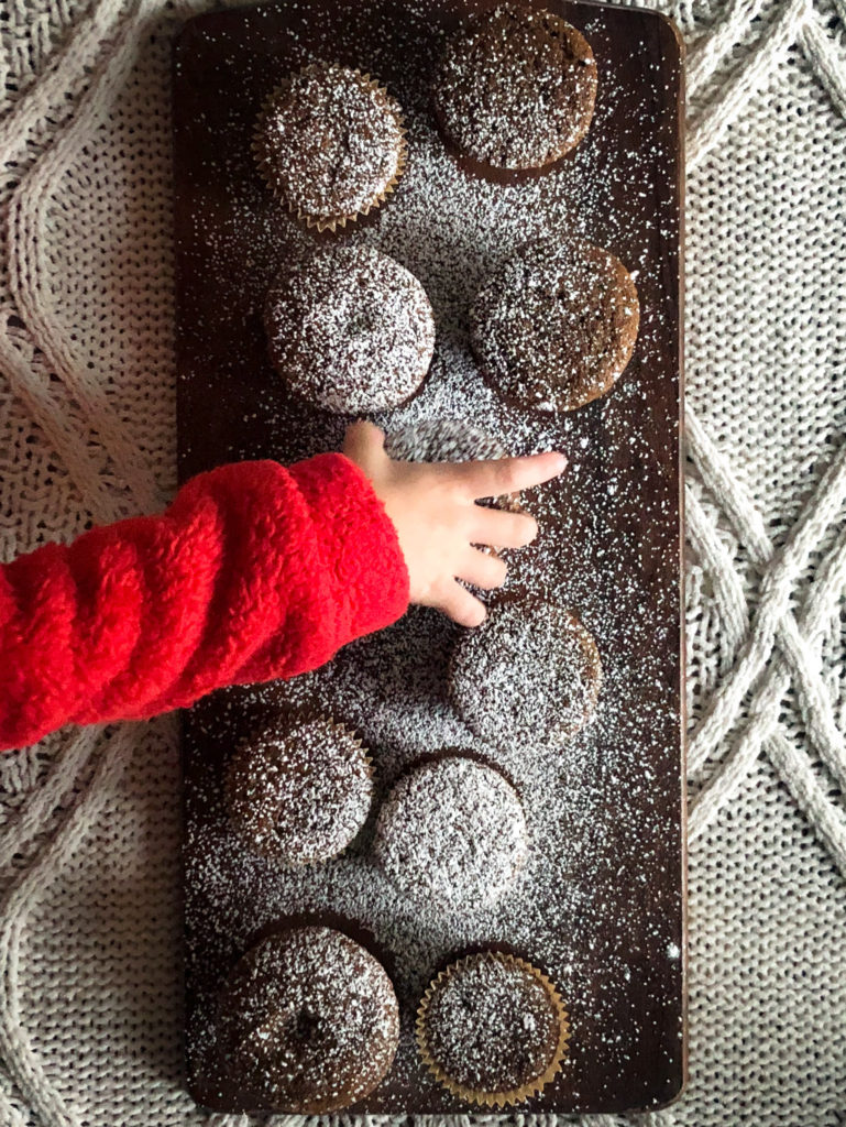 Child reaching for a Gingerbread Muffin dusted with powdered sugar.