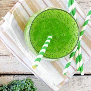 green smoothie in a glass with a green and white stripped paper straw