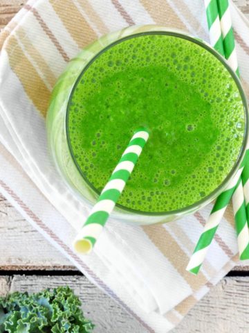 green smoothie in a glass with a green and white stripped paper straw