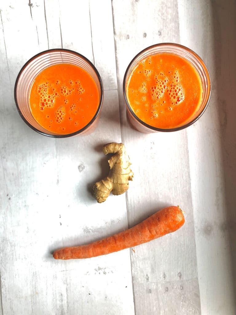 Face made from 2 glasses of ginger carrot smoothie for the eyes, large knob of ginger for the nose, and a carrot for a smiley mouth.