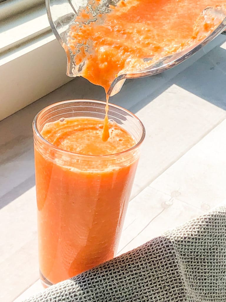 Bright orange carrot ginger smoothie being poured from the blender into a glass.