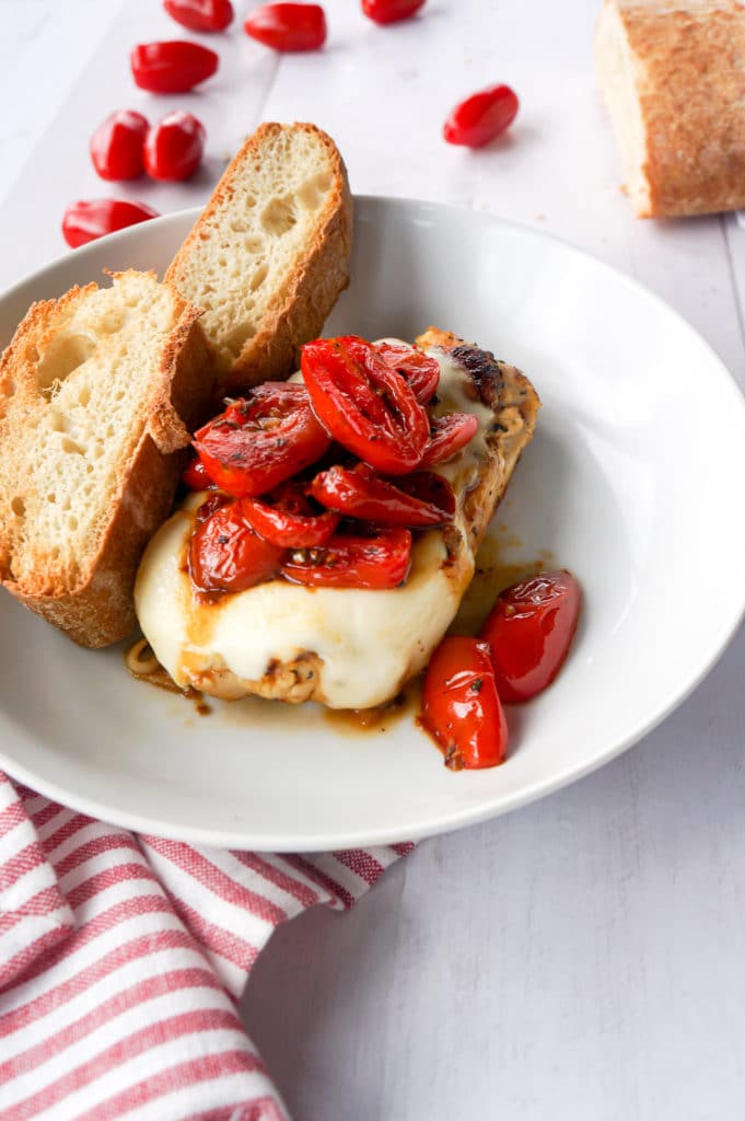 Chicken breast topped with melted cheese and plum tomatoes. Crusty bread on the side. 