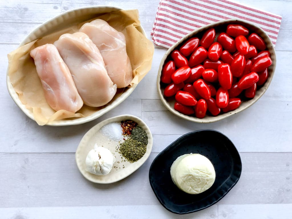 Ingredients for recipe shown. Raw chicken breasts, plum tomatoes, spices, garlic, and fresh mozzarella.