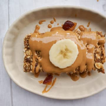 Banana oat bar in a dish topped with peanut butter drizzle and a slice of banana.