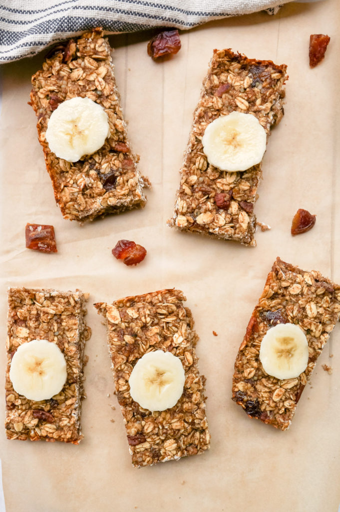 5 banana oat bars on brown baking paper, each topped with a single slice of banana.