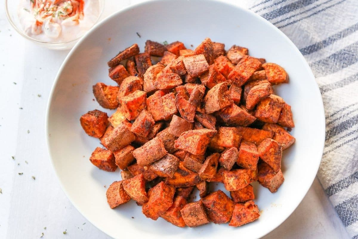 Generously spiced, bright orange sweet potatoes on a white background in a white bowl.