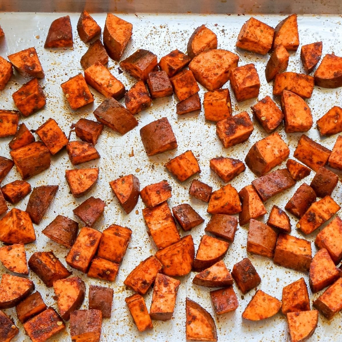 Cubed sweet potatoes, generously spiced on a sheet pan ready to go into a hot oven for roasting.
