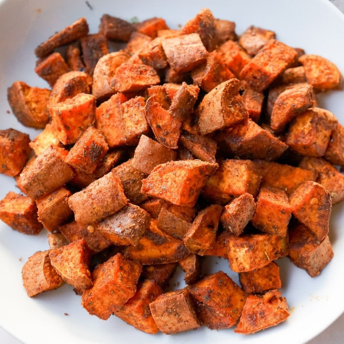 Generously spiced, bright orange sweet potatoes on a white background in a white bowl.