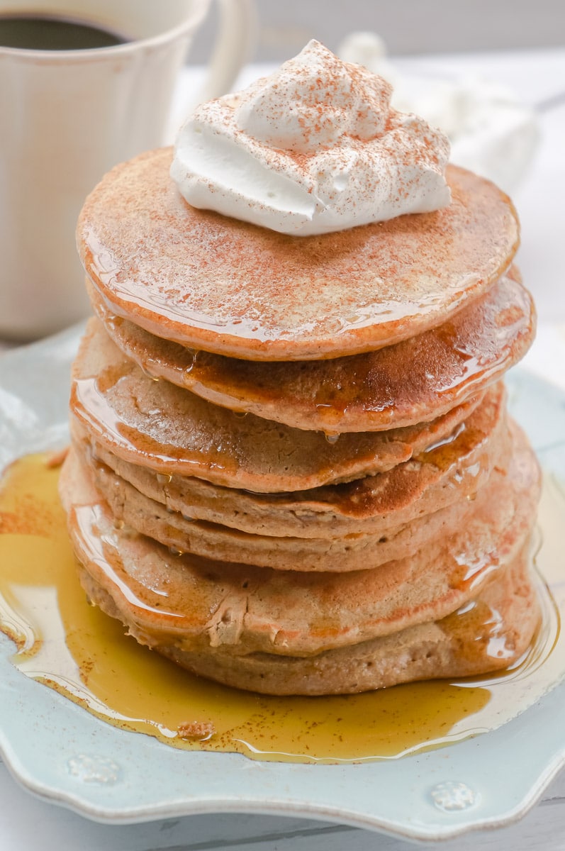 Tall stack of gingerbread pancakes topped with maple syrup, whipped cream, and gingerbread spices.