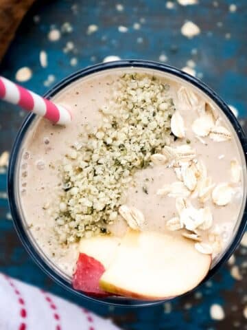 yummy smoothie in a glass topped with hemp hearts, fresh apple slices, and oats.
