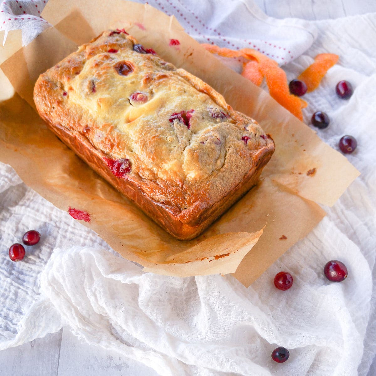 Beautiful loaf of gluten-free holiday cranberry bread with a cream cheese swirl. cranberries and orange peels are seen in the background.