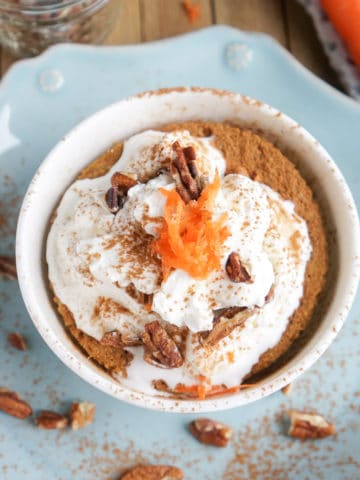 Carrot Cake in a mug topped with whipped cream, cinnamon, pecans, and carrots.