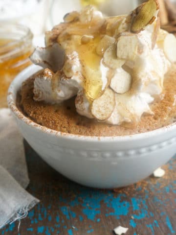 Honey cinnamon mug cake in a white dish then topped with whipped cream, cinnamon, almonds, and extra honey.