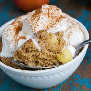 apple cake baked in a small white baking dish. topped with whipped cream and cinnamon.