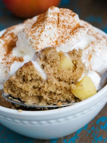 apple cake baked in a small white baking dish. topped with whipped cream and cinnamon.