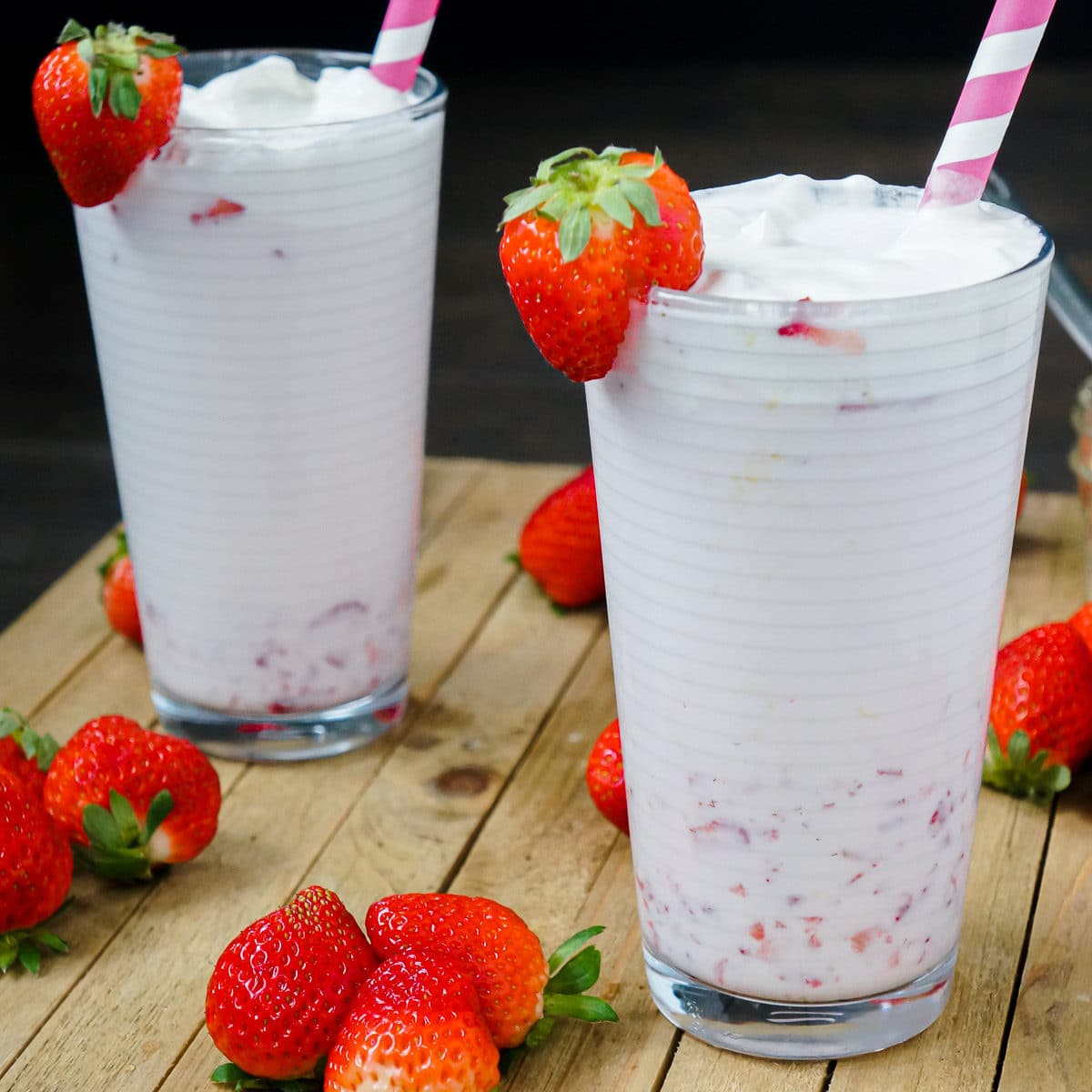 2 glasses of Korean Style strawberry milk with a pink straw and fresh strawberries