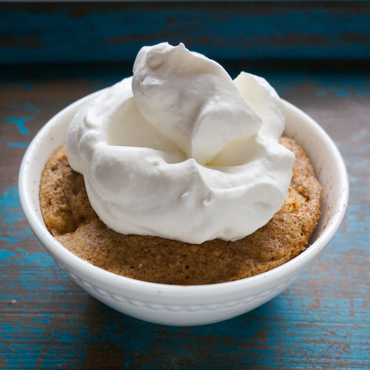 apple mug cake baked in white dish topped with whipped cream