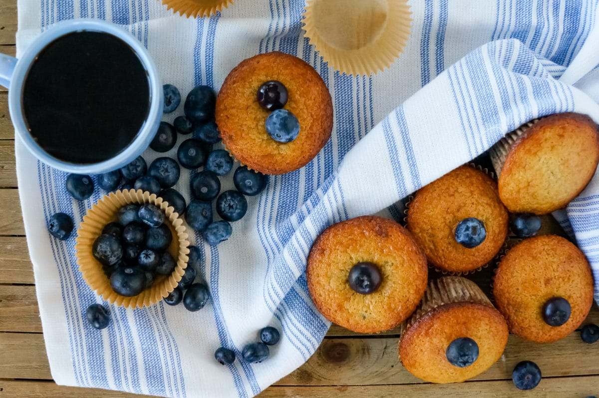 blueberry muffins on a table with fresh blueberries and a cup of coffee