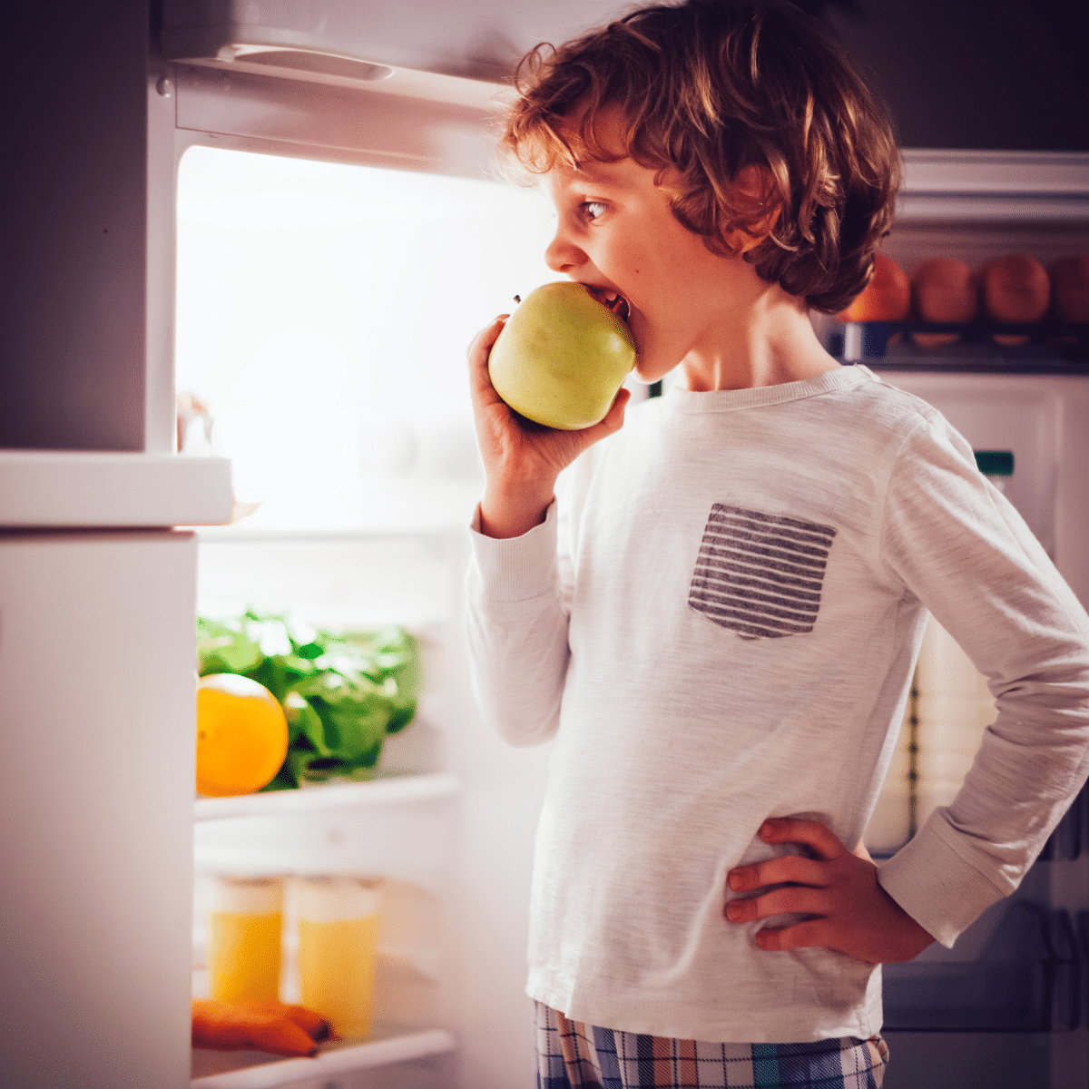 Child in pajamas eating a bedtime snack while standing in front of the refrigerator