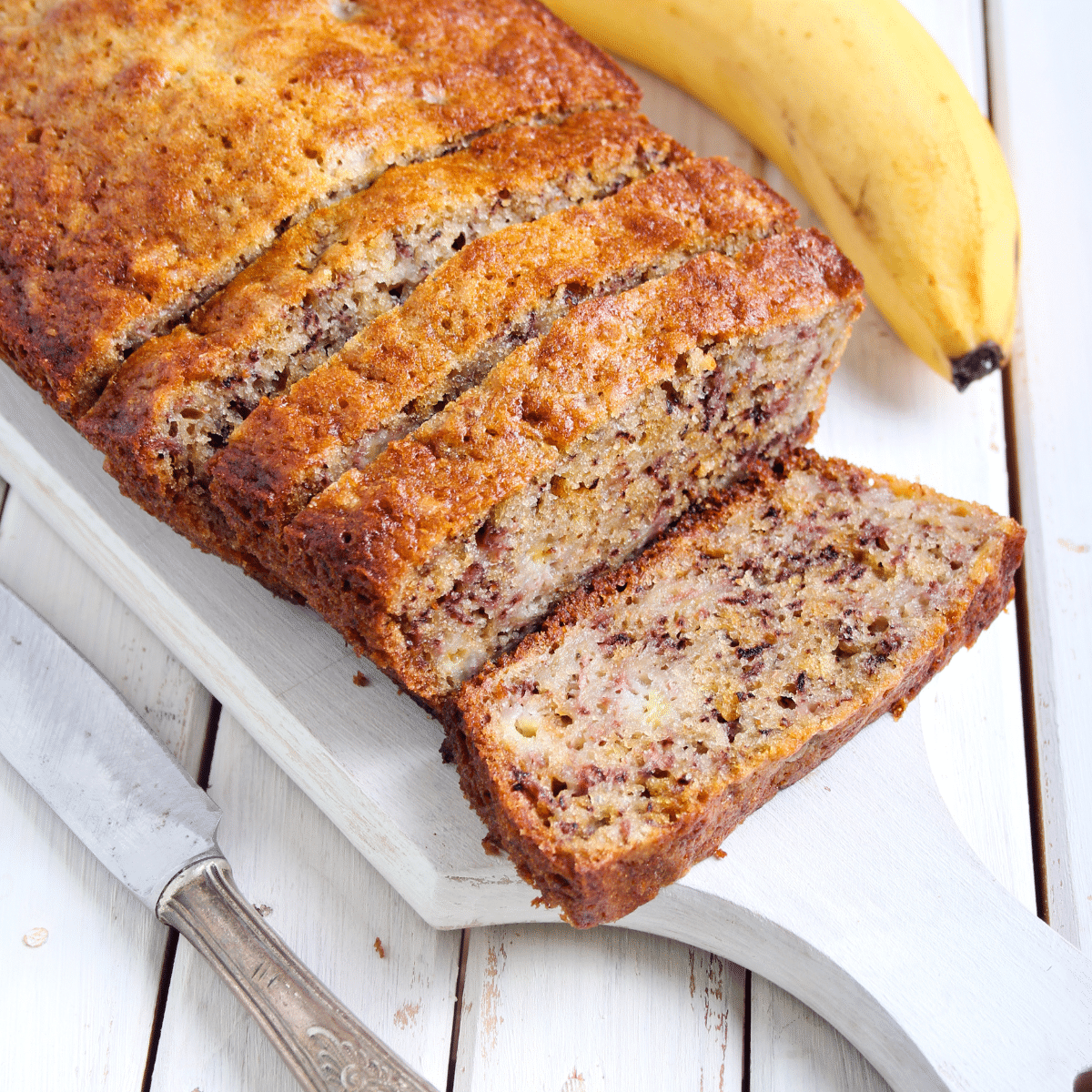 Homemade banana nut bread loaf cut into slices on a white wooden board.