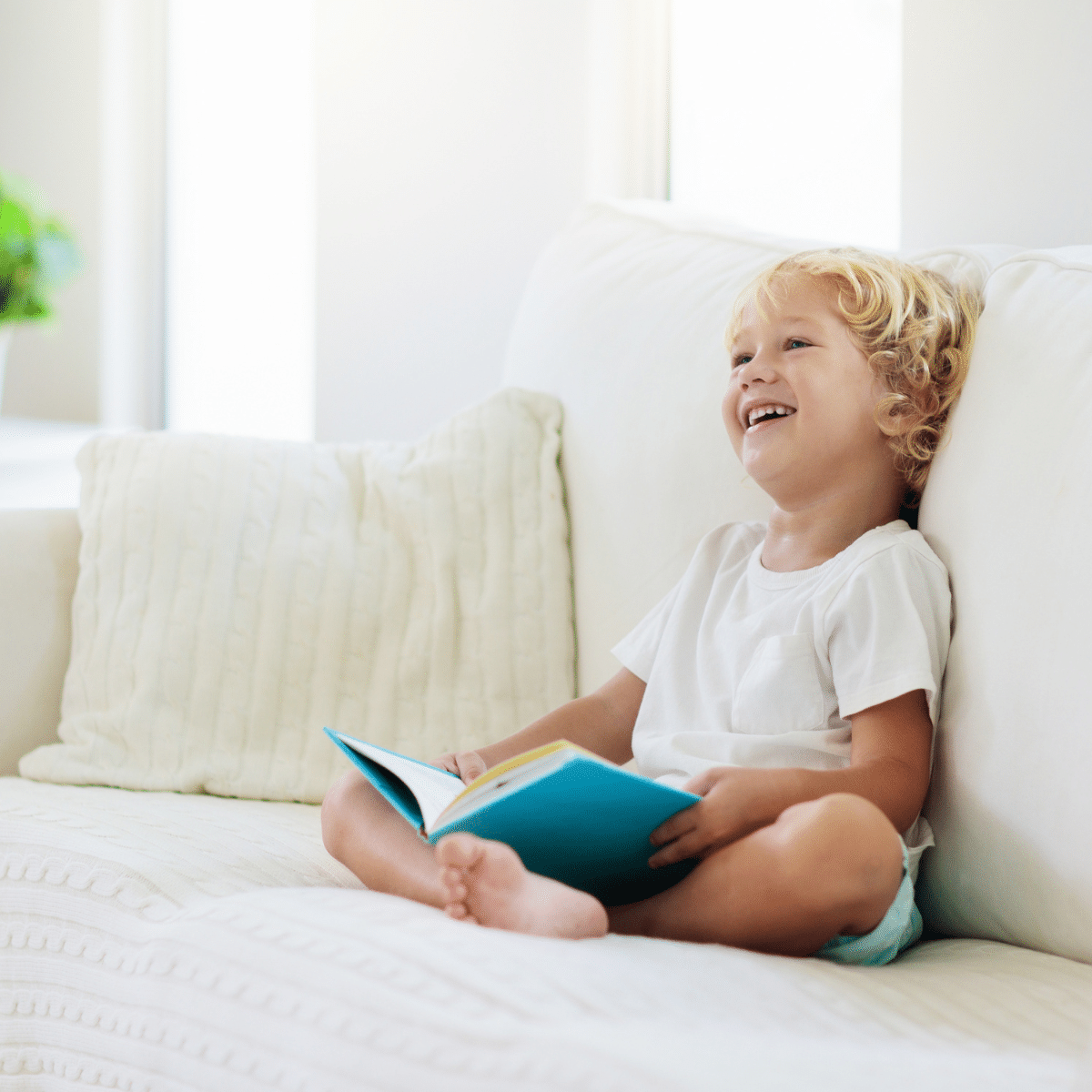 Child sitting on a couch laughing while reading a book