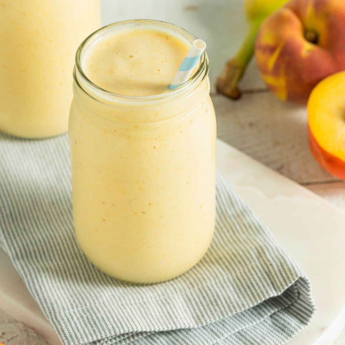 A cold and creamy pineapple peach smoothie in a clear glass cup with a blue and white striped straw.